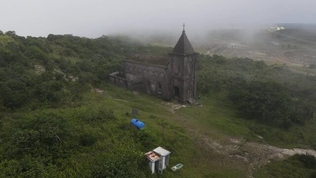 Iconic old church built by french colon in the early XXth located on the top of Bokor mountain in Cambodia. Drone is moving backward showing the landscape under fog and clouds.