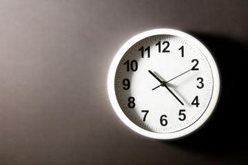 Close-up of a  modern fashioned white Wall Clock with numerals on the clock face. Clock with white frame on a black background. Pointers showing the time.  front view of the Watch out of center