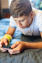 Cute boy with broken hand relaxing and smiling on couch. Close up young handsome Teenage with with yellow plaster playing smartphone at home. 