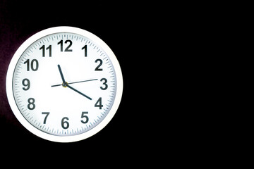 Close-up of a  modern fashioned white Wall Clock with numerals on the clock face. Clock with white frame on a black background. Pointers showing the time.  front view of the Watch out of center