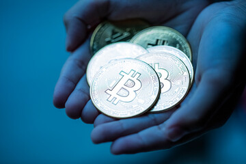 Shiny bitcoins in hand palm over dark blue background. Cryptocurrency market crash concept.