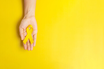 hand holding Yellow Ribbon on yellow background for supporting people living and illness. Suicide prevention day, Sarcoma cancer and Childhood Cancer Awareness month concept - obrazy, fototapety, plakaty