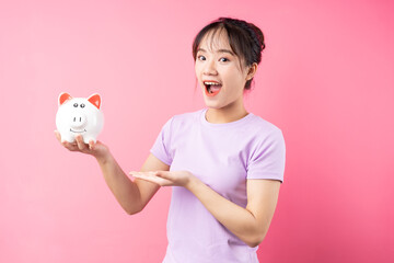 Fototapeta na wymiar Portrait of girl holding piggy bank in hand, isolated on pink background