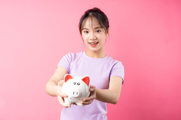 Fototapeta na wymiar Portrait of girl holding piggy bank in hand, isolated on pink background