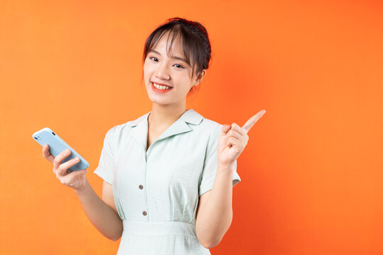Portrait of young girl using phone and pointing to the right, isolated on orange background
