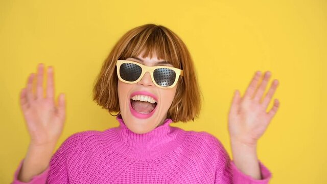 A girl standing in front of a yellow background with short hair and a pink sweater grimaces while, she is wearing Anti Fatigue glasses. The Vision Pinhole Pinhole.