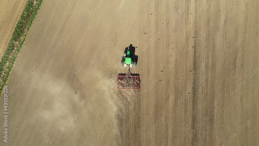 Poster tracking aerial top down zoom out view of green tractor cultivating agricultural field. tractor turn