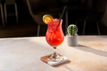 A view of a red colored alcoholic beverage in a hurricane shaped glass.
