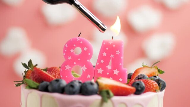 Birthday cake candle number 84. Candle and cake on pink background and fire by lighter. Close-up and slow motion