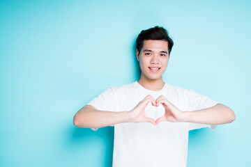 Handsome asian guy showing heart with hands and smiling while looking at camera