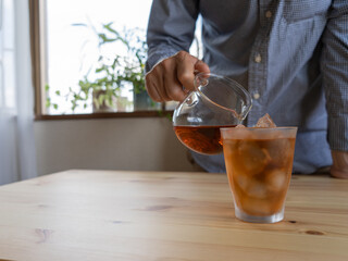 氷の入ったグラスに紅茶を注ぐ男性。