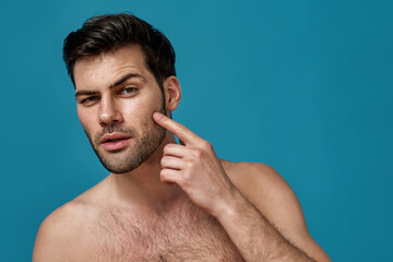 Portrait of shirtless handsome caucasian man checking his facial skin isolated over blue background