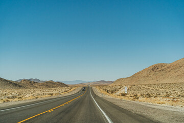 Fototapeta na wymiar Desert highway road leading to the horizon against clear blue sky and mountains