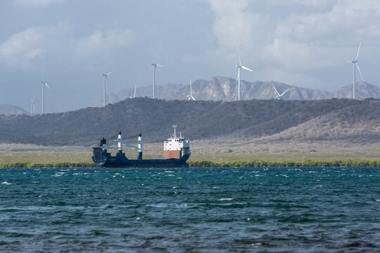Dramatic image of a empty cargo ship in the Caribbean bay with wind power turbines in the mountains of the background in the Dominican Republic.