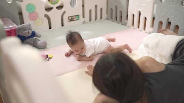 asian baby infant learning crawling skill development by mother woman encourage at home. parent mother assist helping baby crawl lesson. authentic life at home. baby infant playing in playpen. 
