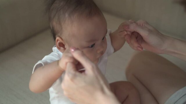 woman mother hand assist baby infant pull up to sit. mother teaching lesson to baby to develop skill at home. baby successful sit up with mother helping. 4 months baby skill improvement.