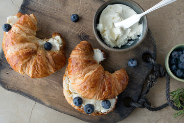 flat lay croissants with cream cheese and berries on wooden board