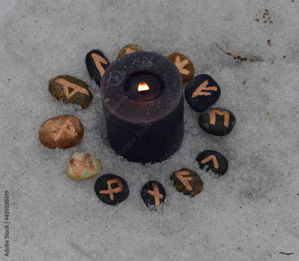 Wall mural Close up of black candle and runes in snow.