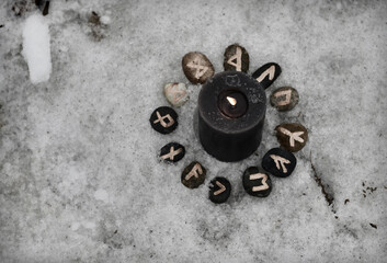 Top view of black burning candle with runes and copy space against snow.