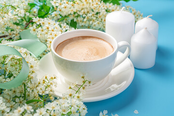 White cappuccino coffee cup and flowers close-up on light blue background.