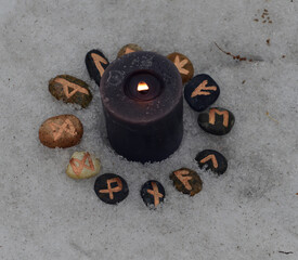 Close up of black candle and runes in snow.