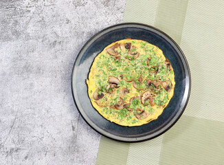 Mushroom Omelet with herbs on a round plate on a dark grey background. Top view, flat lay