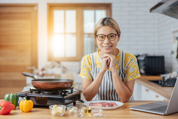 happy young woman smiling in a modern kitchen. beautiful Asian woman stands in a kitchen cooking wearing a red apron. The healthy menu she will cook is salmon, steak and salad.