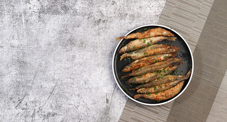 Pan fried capelin or smelt fish on a round plate on a dark grey background. Top view, flat lay