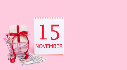 A gift box in a shopping trolley, dollars and a calendar with the date of 15 november on a pink background.