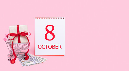 A gift box in a shopping trolley, dollars and a calendar with the date of 8 october on a pink background.
