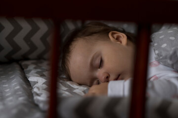 Cute cheerful little chubby baby girl sleeping sweetly in grey baby crib during lunch rest time in...