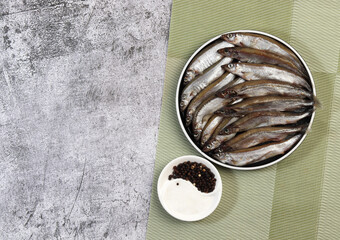 Raw capelin on a round plate on a dark grey background. Top view, flat lay