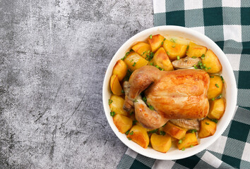 Whole Roasted Chicken with potatoes in a white baking dish on a dark grey background. Top view, flat lay .