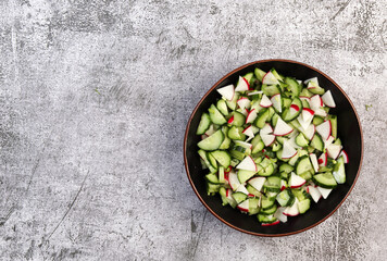 Cucumber and radish salad in a bowl  on a dark grey background. Top view, flat lay