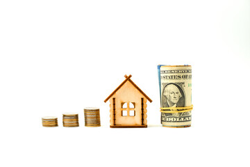 Miniature toy wooden house, US dollars rolled into a tube, stacks of metal coins isolated on a white background. Сoncept of buying and selling apartments, houses. Real estate object. Copy space.