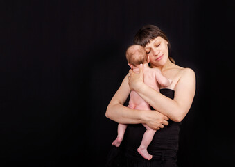 Naklejka premium Newborn baby with mommy. Love of a mother and baby. Family. Smiling baby and his mom. Young mother holding her newborn child in hands. Caucasian mom holding her cute infant on the black background.