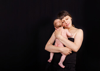 Newborn baby with mommy. Love of a mother and baby. Family. Smiling baby and his mom. Young mother holding her newborn child in hands. Caucasian mom holding her cute infant on the black background.