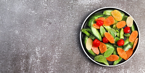 Candied pomelo, pineapple, kumquat on a round plate on a dark background. Top view, flat lay