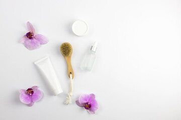 Cosmetic layout, ready-made template for advertising face care products. White tubes with cream and a brush for facial massage on a white background with orchid flowers.