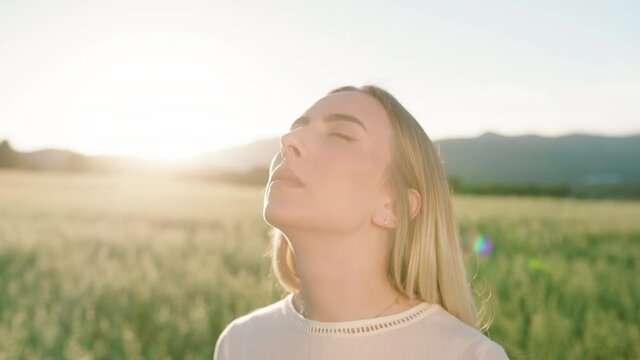 Close up shot of young woman with closed eyes enjoying sunbeams in rural nature
