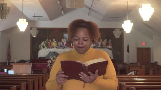 Young African American woman happily reading the bible in empty church during lockdowns