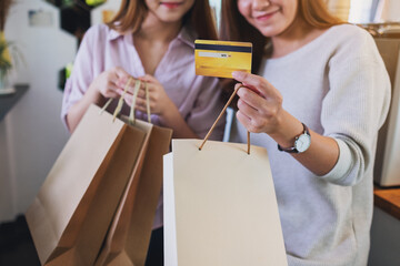 Closeup image of two young women holding shopping bags and a credit card for purchasing