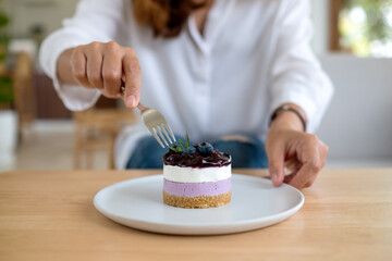 Closeup image of a woman holding and eating a piece of blueberry cheesecake