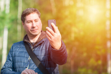 One 40s man with his mobile smart phone searching for reception signal in the sunny forest.