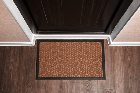 Blank Doormat Before The Dark Door In The Hall. Top View Of Mat On Wooden Floor. Mockup For Your Design