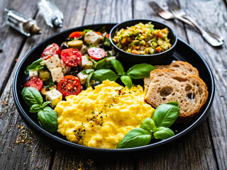 Continental breakfast - scrambled eggs, bread and greek salad on wooden table
