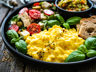 Continental breakfast - scrambled eggs, bread and greek salad on wooden table

