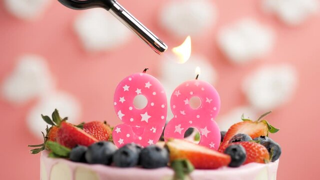 Birthday cake candle number 98. Candle and cake on pink background and fire by lighter. Close-up and slow motion