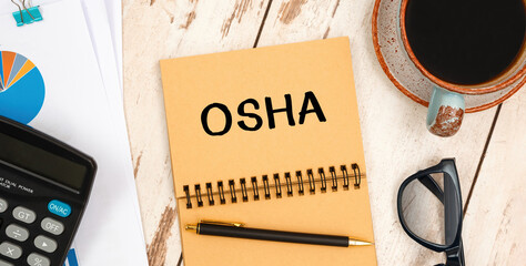 Naklejka premium Notebook with text OSHA - Occupational Safety and Health Administration - near office supplies.