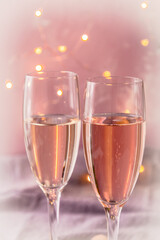 Two glasses with sparkling wine on pink pastel background with fairy lights in romantic atmosphere